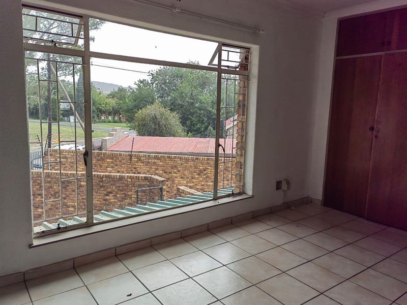 An empty bedroom featuring tiled flooring, a large metal-framed window with security bars, and a built-in wooden wardrobe.