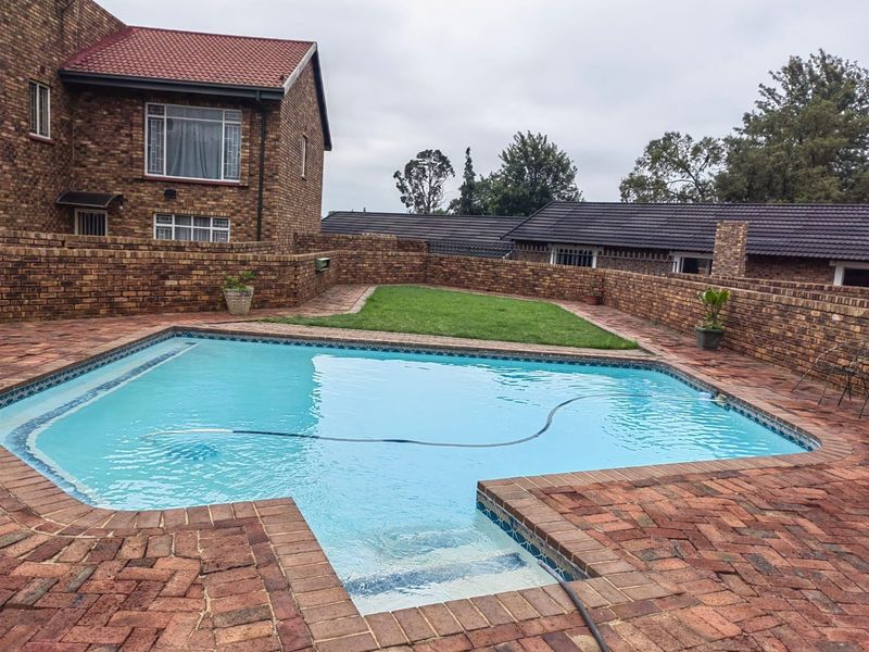 A private outdoor pool area featuring a swimming pool, brick paving, and a small lawn enclosed by a brick boundary wall.