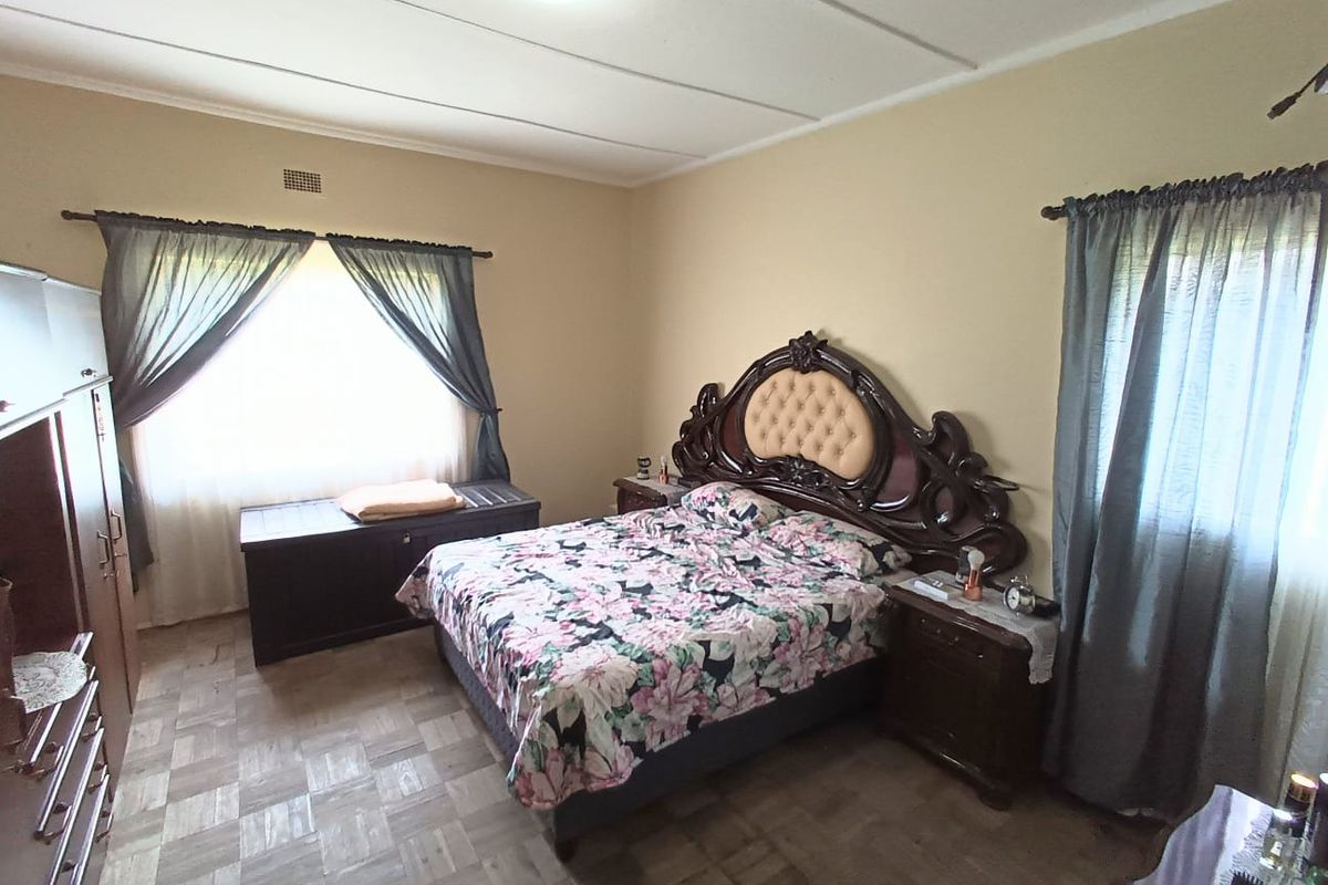 A spacious bedroom featuring parquet flooring and natural light from dual windows.