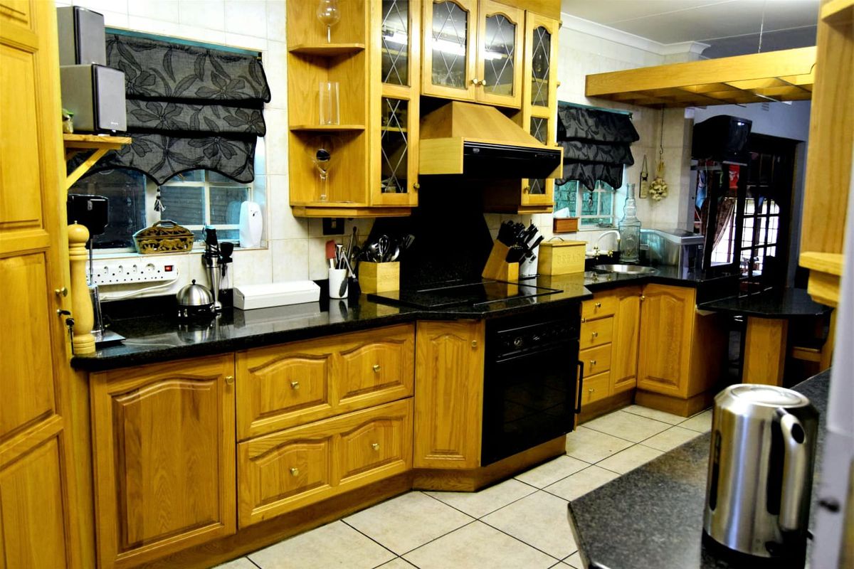 A traditional kitchen featuring wooden cabinetry, dark granite countertops, a built-in oven, and a black extractor fan, with tiled flooring throughout.