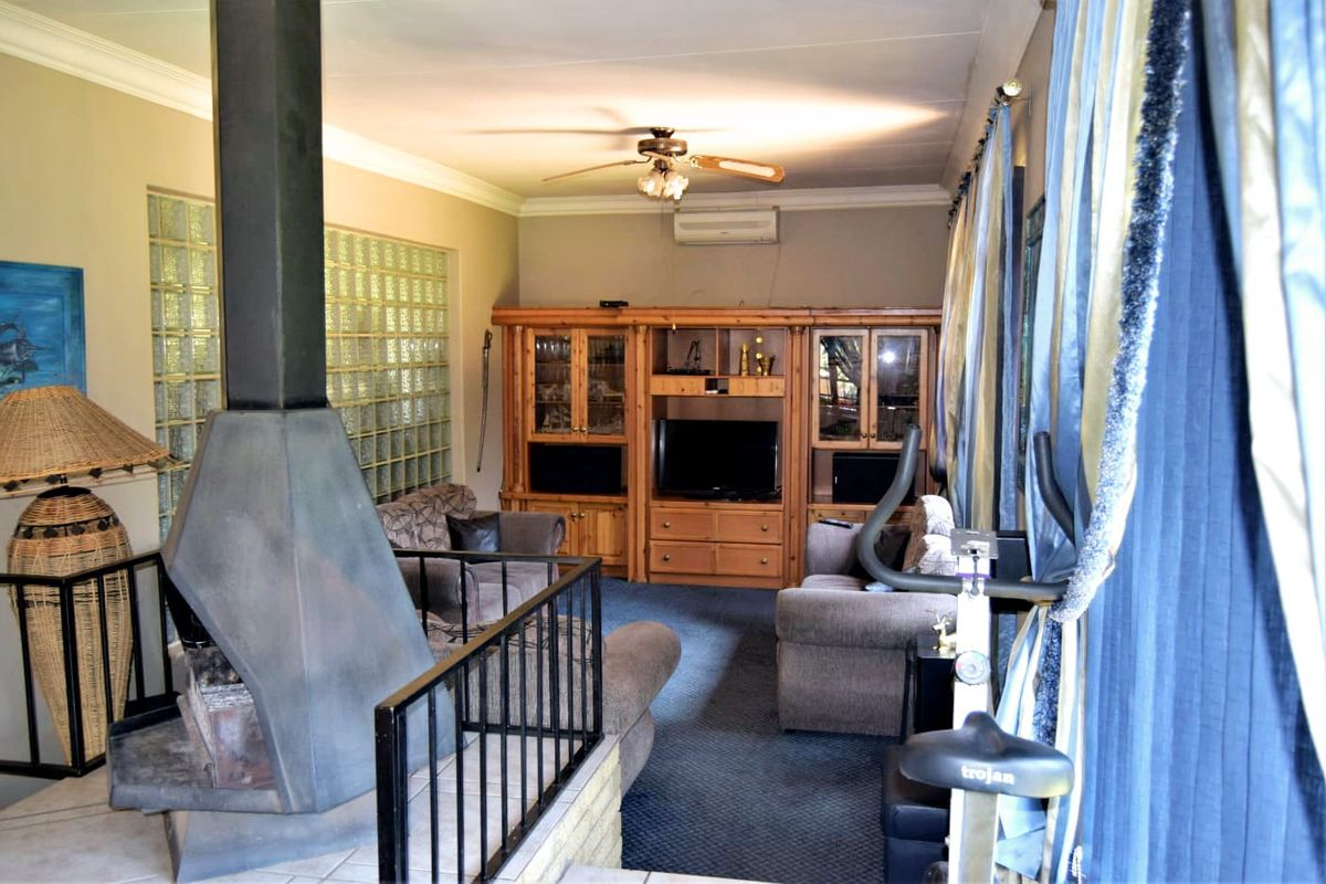 A living room featuring a central freestanding fireplace, glass block feature wall, built-in wooden cabinetry, and a ceiling fan.