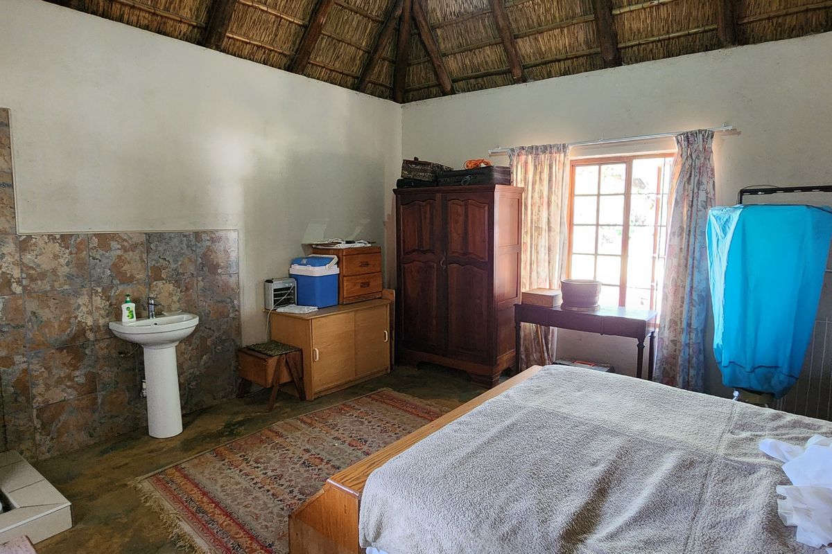 A bedroom featuring a traditional thatched roof, a pedestal basin with tiled splashback, and timber-framed windows.