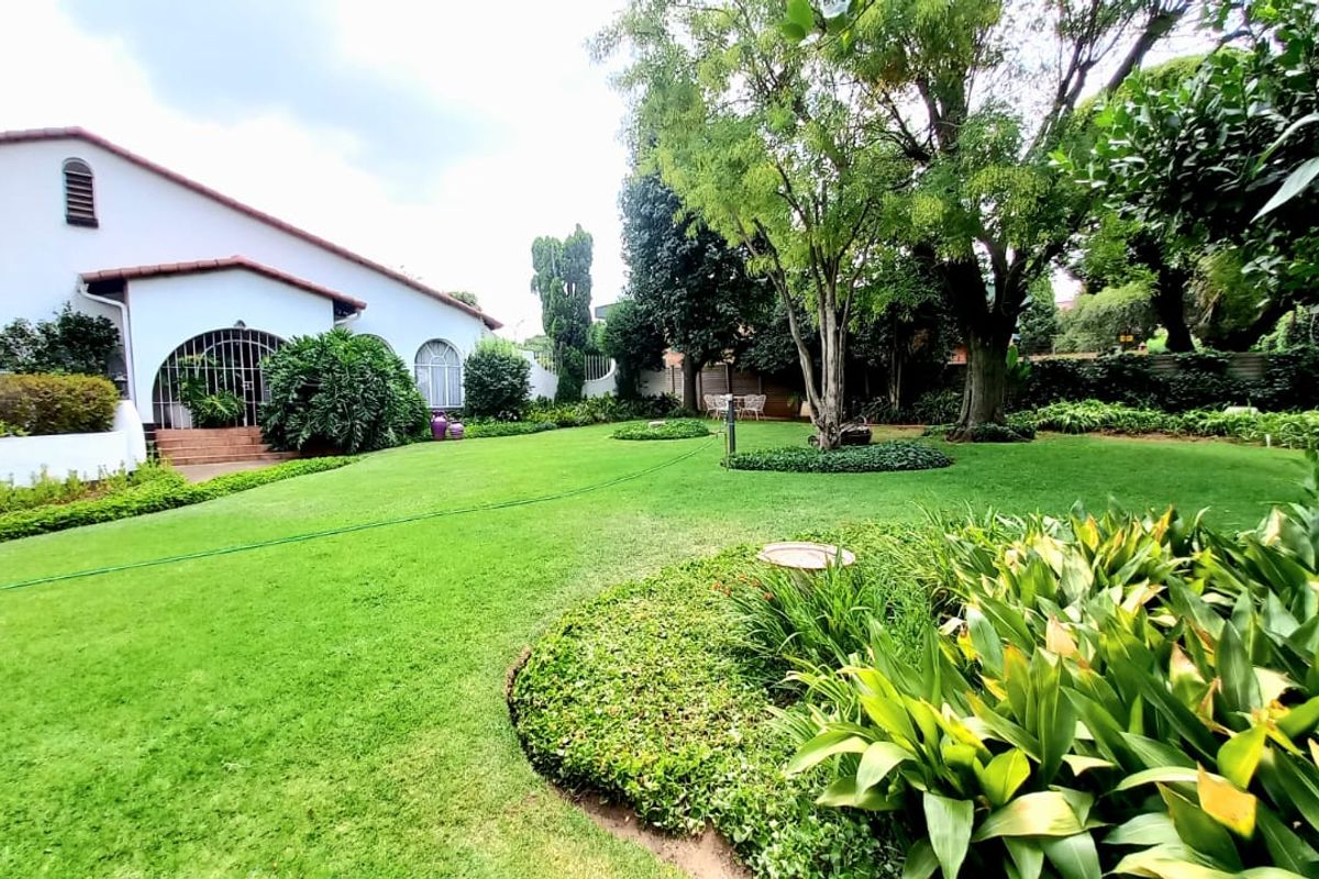 A spacious, well-maintained rear garden featuring a large manicured lawn, mature trees, and established landscaped garden beds adjacent to the house.