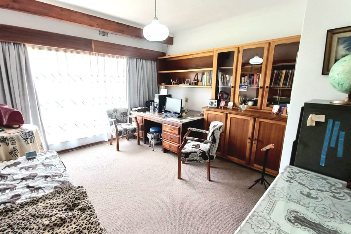 A multi-purpose bedroom featuring built-in wooden cabinetry, shelving, and a desk area with large windows providing natural light.
