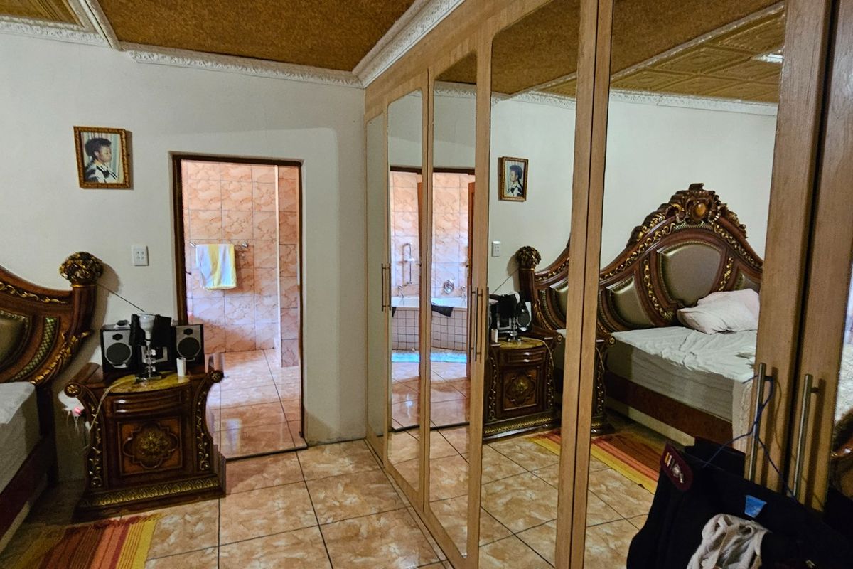 A bedroom featuring large mirrored built-in wardrobes, tiled flooring, and an en-suite bathroom access.
