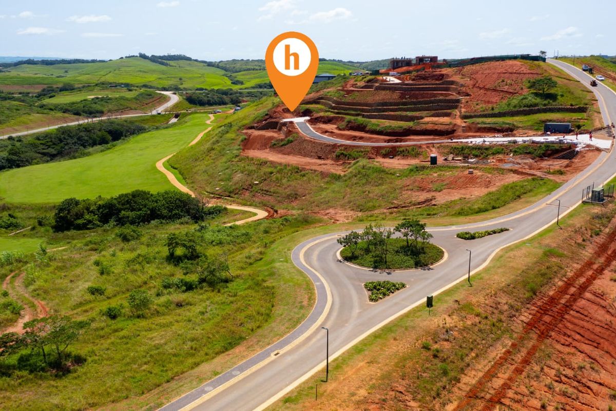 Aerial view of a developing residential estate featuring paved roads, a roundabout, and terraced land plots ready for construction.