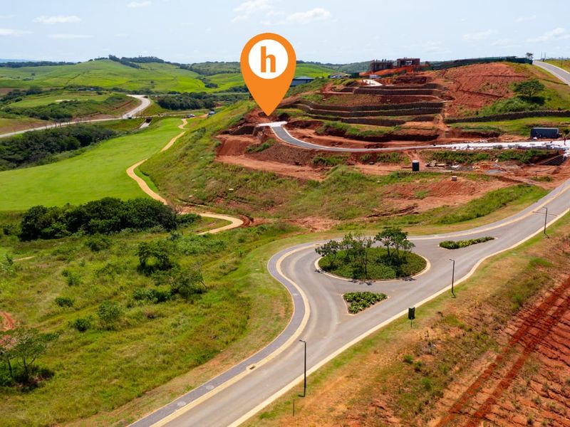 Aerial view of a developing residential estate featuring paved roads, a roundabout, and terraced land plots ready for construction.