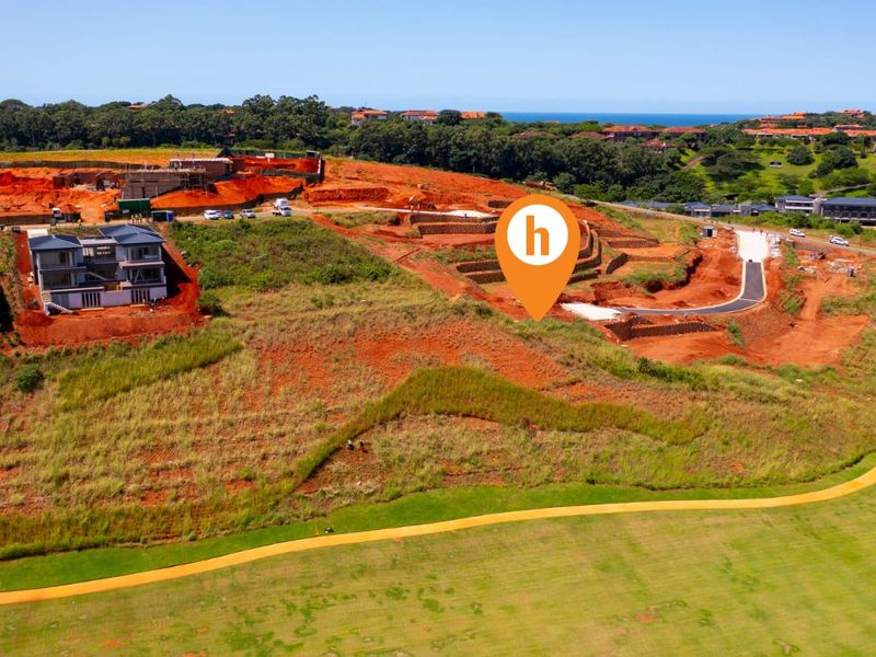 Aerial view of a residential development site featuring cleared plots, paved access roads, and surrounding coastal landscape.