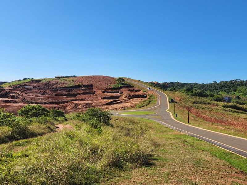 An elevated view of a developing estate featuring paved roads, a roundabout, and ongoing earthworks on the surrounding hillside.