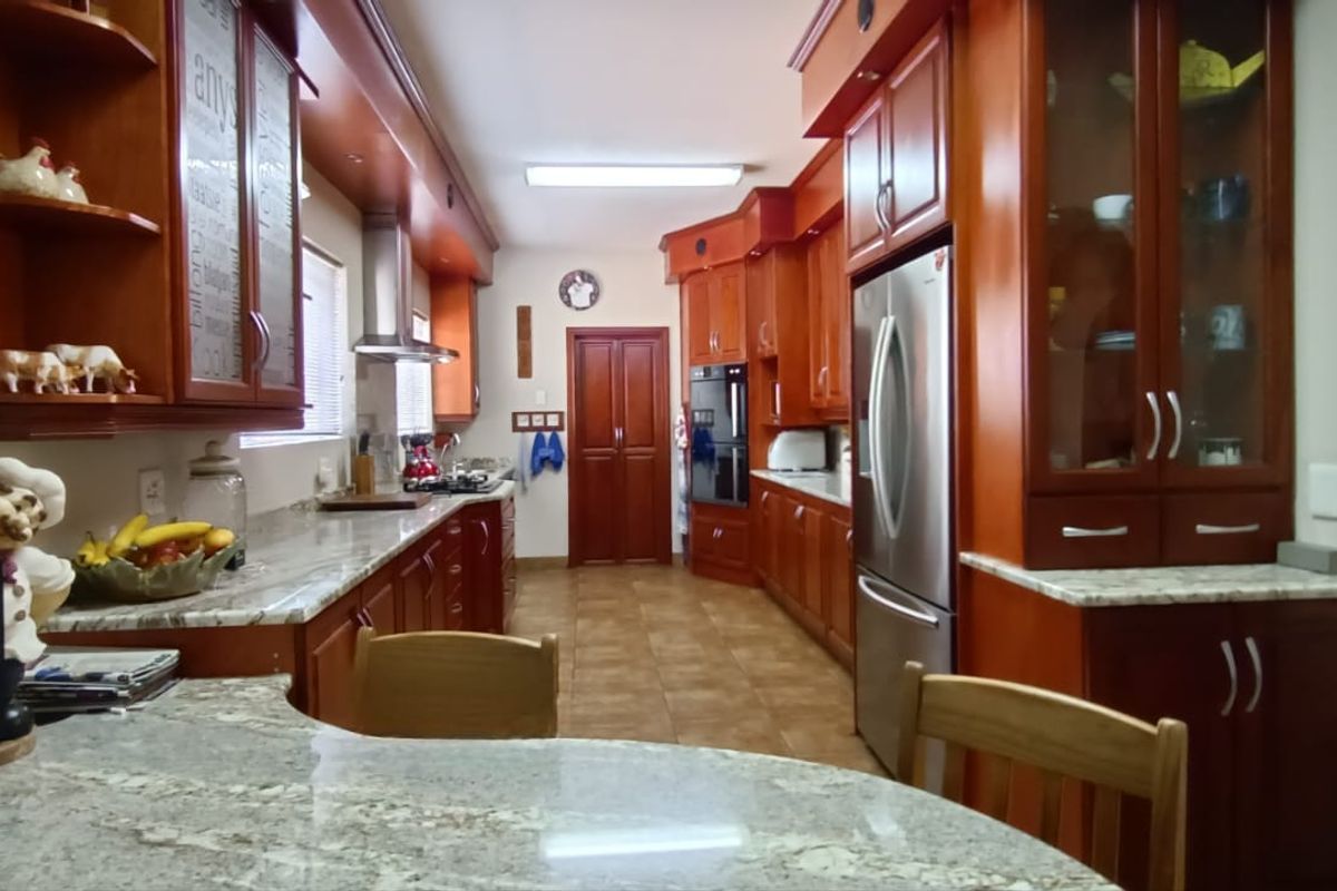 A spacious kitchen featuring extensive cherry wood cabinetry, granite countertops, built-in oven, and stainless steel extractor fan with tiled flooring.