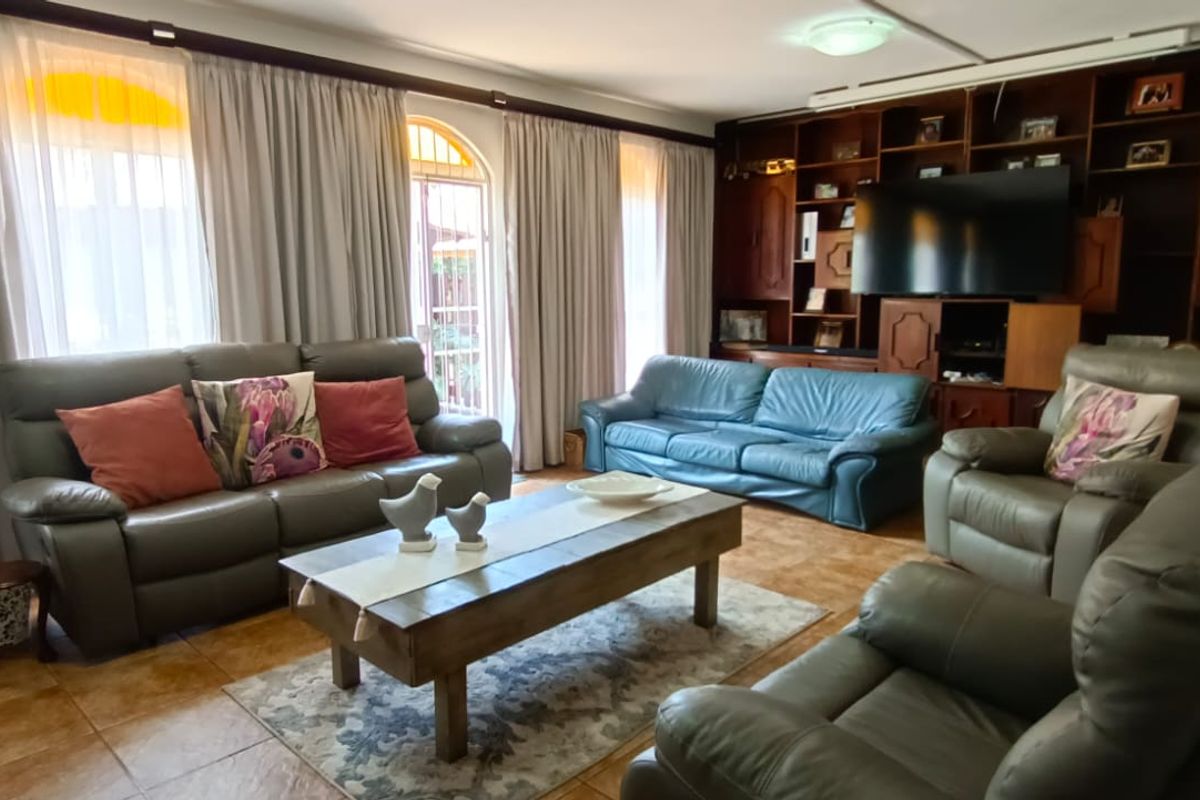 A spacious living room featuring built-in wooden cabinetry, tiled flooring, and large windows with floor-to-ceiling curtains.