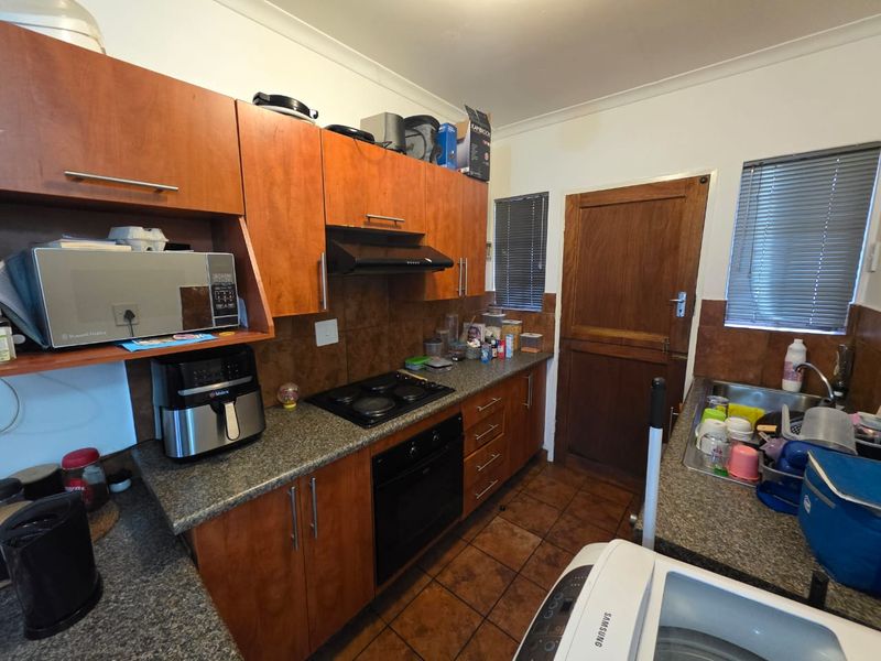 Functional kitchen featuring wood-finish cabinetry, granite-look countertops, built-in oven and hob, tiled backsplash, and direct access to an exterior door.