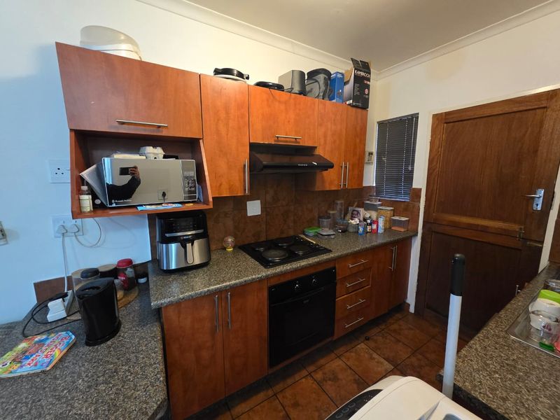 A functional kitchen featuring wood-finish cabinetry, granite-look laminate countertops, a built-in oven, electric hob, and tiled flooring.