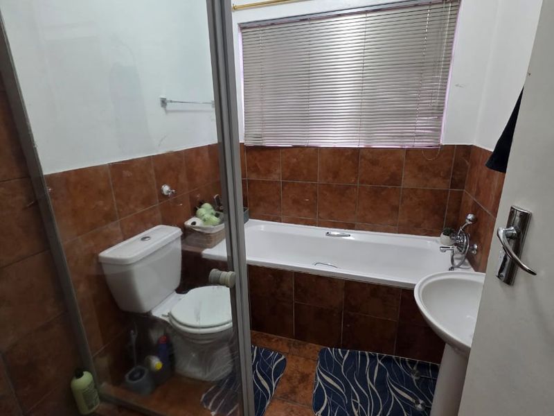 A functional bathroom featuring a bathtub, separate shower enclosure, pedestal basin, and toilet, finished with brown wall and floor tiles.