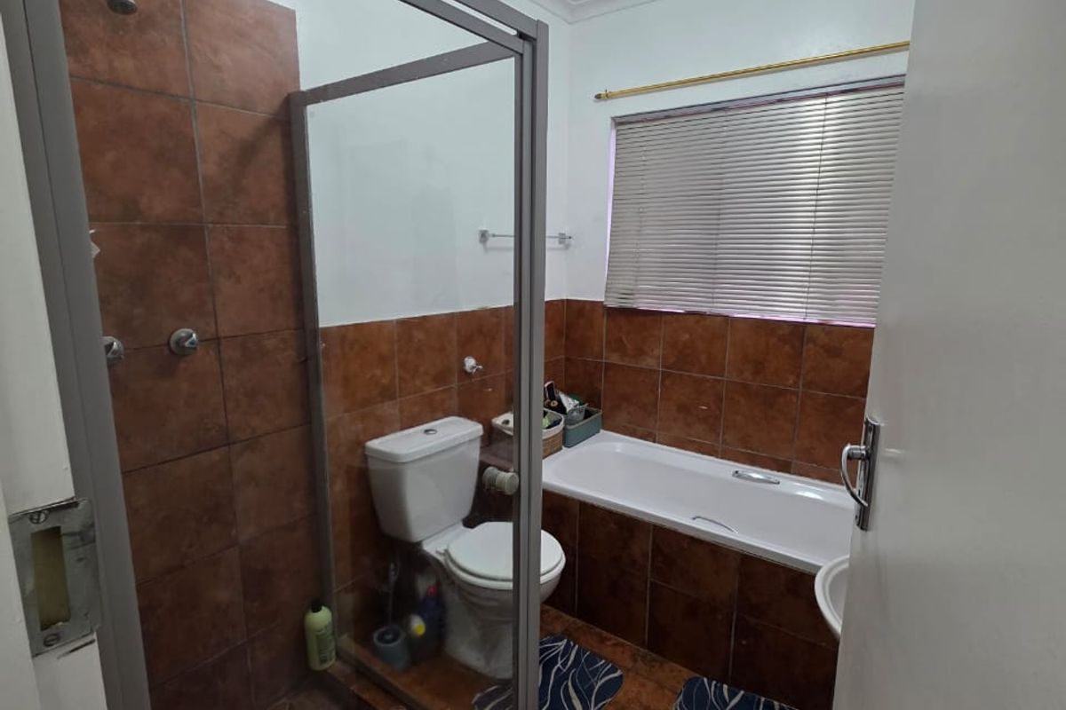 A functional bathroom featuring a separate shower enclosure, bathtub, toilet, and tiled finishes throughout, offering a dated but practical layout.