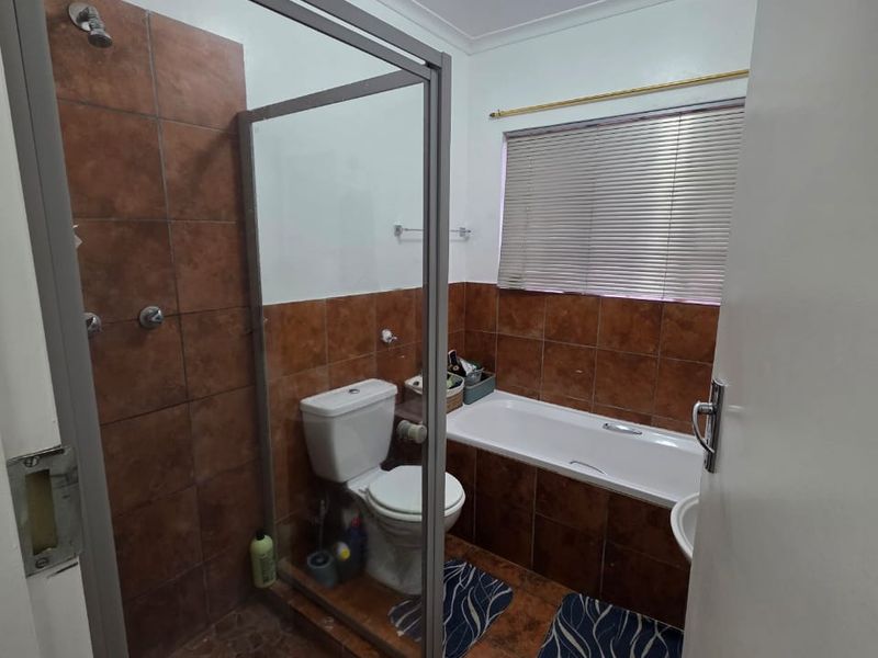 A functional bathroom featuring a separate shower enclosure, bathtub, toilet, and tiled finishes throughout, offering a dated but practical layout.