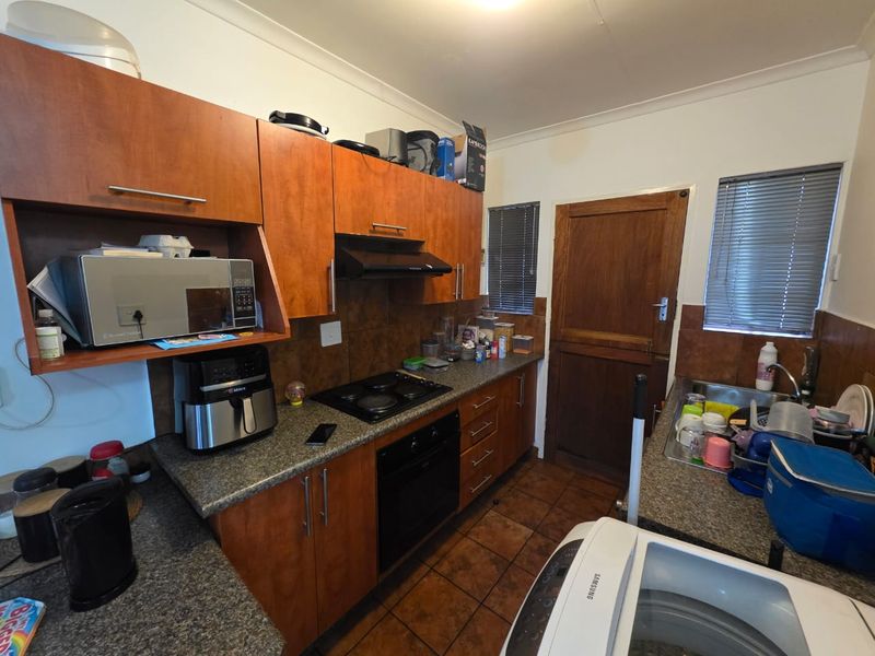 Functional kitchen featuring wood-finish cabinetry, built-in oven and hob, tiled backsplash, and direct access to an exterior door.