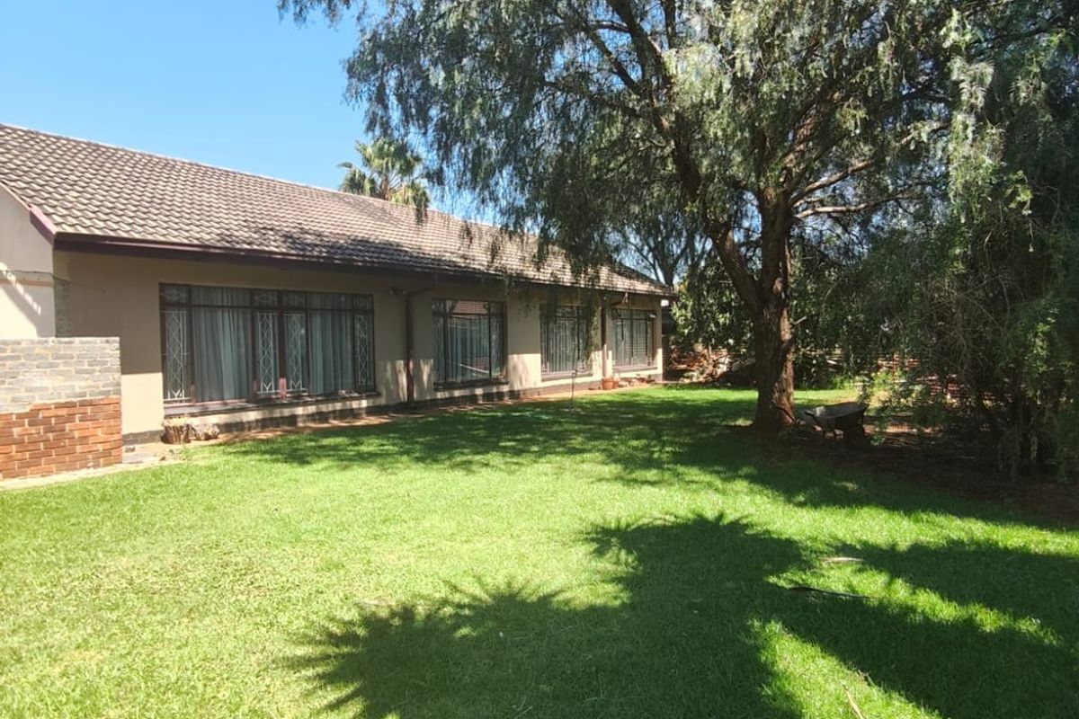 A view of the rear garden featuring a well-maintained lawn, mature trees, and the rear elevation of the house with large windows.