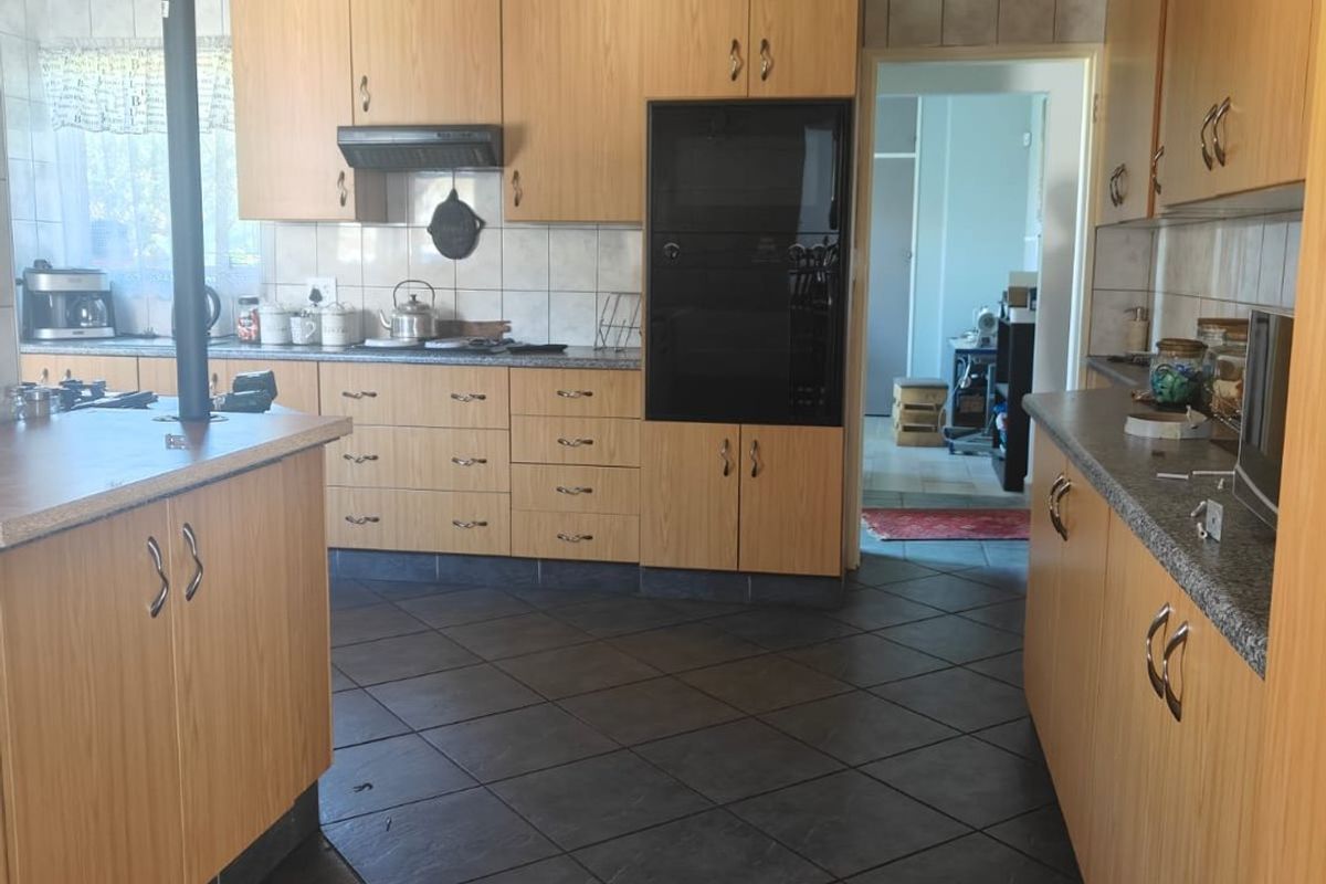 A functional kitchen featuring wood-look cabinetry, dark tiled flooring, a built-in oven, and a central island, offering a practical layout for daily meal preparation.