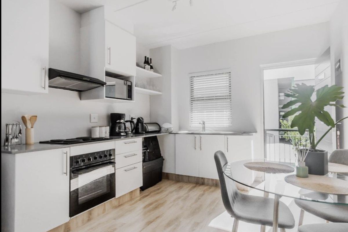 Modern kitchen featuring white cabinetry, integrated oven and hob, stainless steel sink, and light wood-look laminate flooring with access to a balcony.