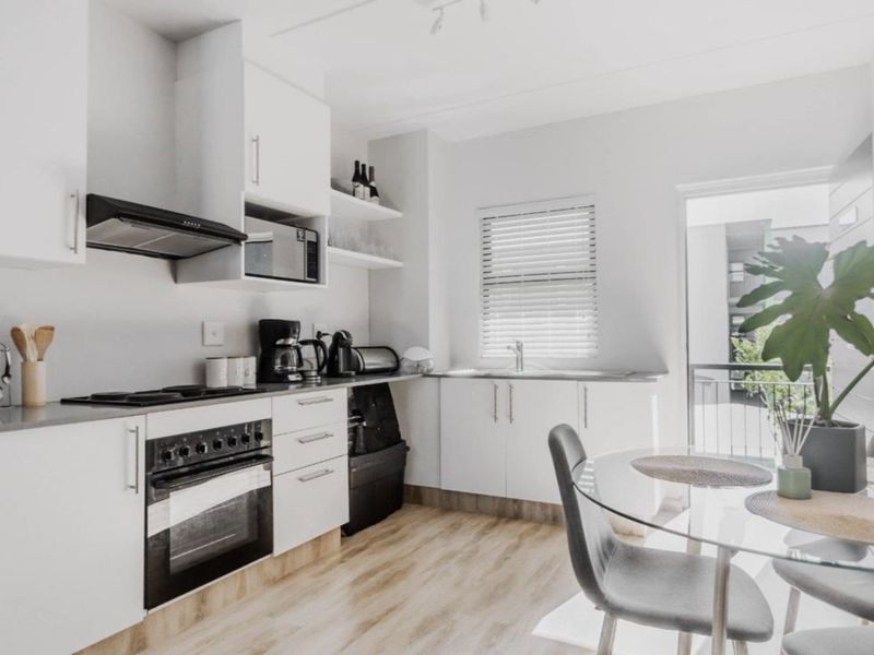 Modern kitchen featuring white cabinetry, integrated oven and hob, stainless steel sink, and light wood-look laminate flooring with access to a balcony.