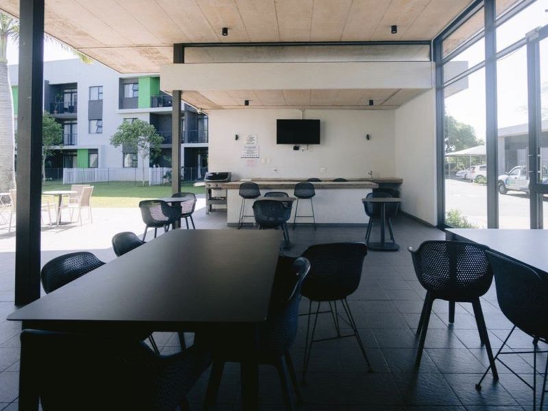 A spacious covered patio area featuring tiled flooring, a built-in bar counter, and large glass sliding doors overlooking the complex grounds.