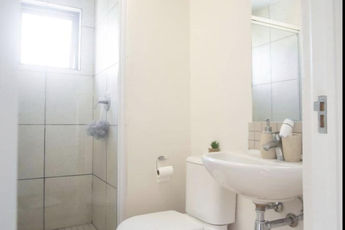 A compact, functional bathroom featuring a glass-enclosed shower, wall-mounted basin, and toilet with light-toned laminate flooring and neutral wall finishes.