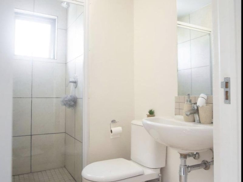 A compact, functional bathroom featuring a glass-enclosed shower, wall-mounted basin, and toilet with light-toned laminate flooring and neutral wall finishes.