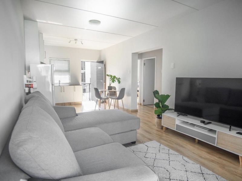 An open-plan living area featuring laminate flooring, a compact kitchen space, and direct access to an outdoor balcony area.