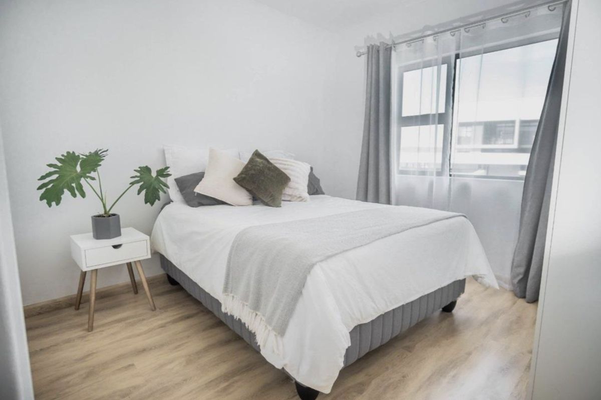 A bright and well-maintained bedroom featuring light-toned laminate flooring and a large window with modern aluminium frames.