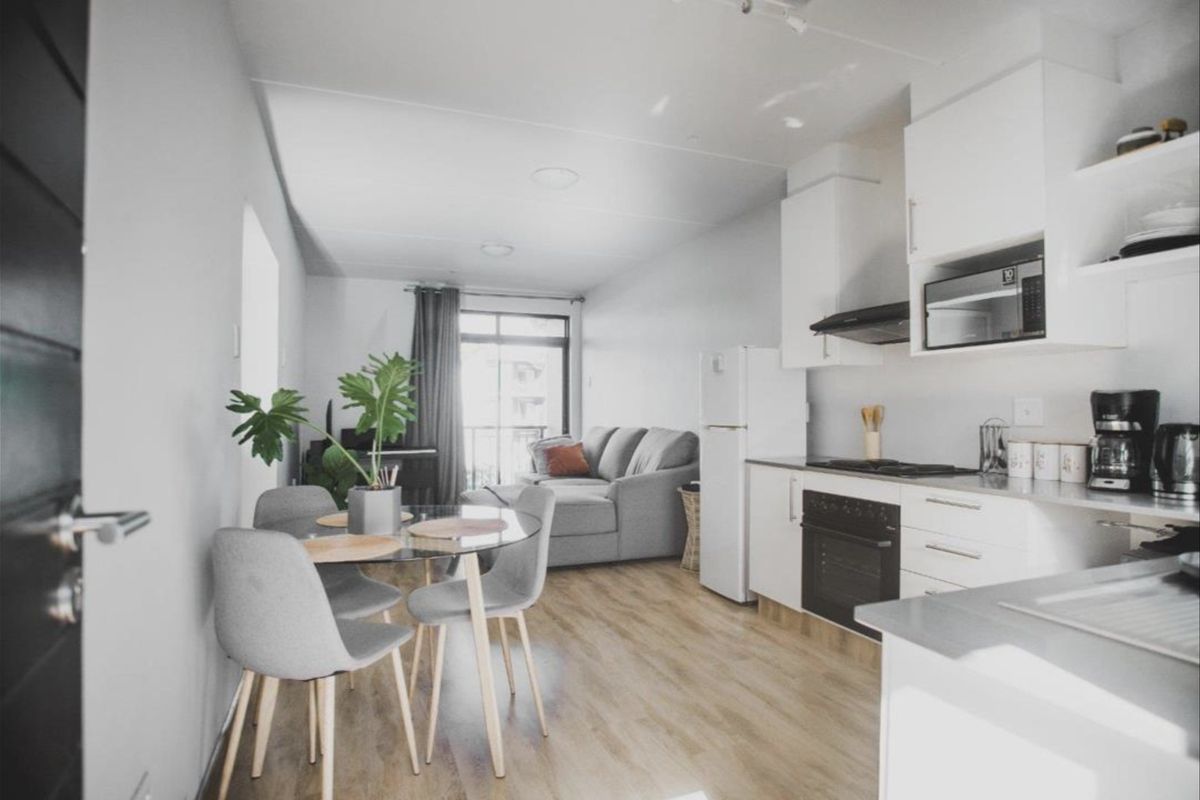 Modern open-plan living area featuring a contemporary kitchen with built-in appliances and light laminate flooring, leading to a balcony.