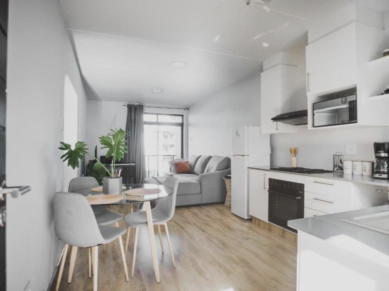Modern open-plan living area featuring a contemporary kitchen with built-in appliances and light laminate flooring, leading to a balcony.
