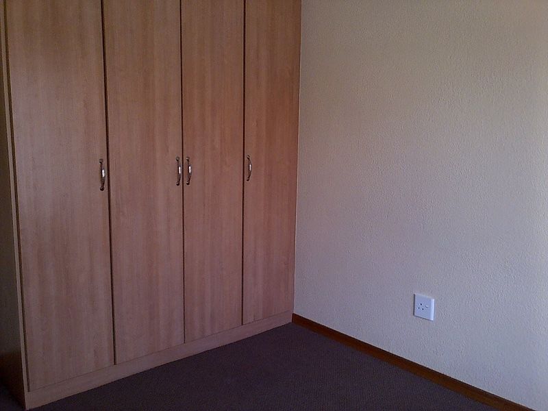 A bedroom interior featuring built-in wooden cupboards and neutral wall finishes, providing a clean and functional space.