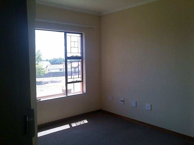 An empty bedroom featuring carpeted flooring, a steel-framed window, and neutral wall finishes, providing a blank canvas for potential interior design.