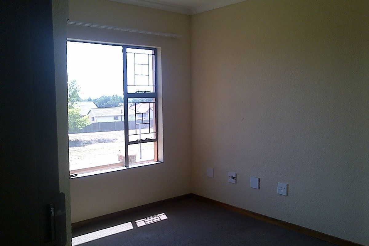 An empty bedroom featuring carpeted flooring, a steel-framed window, and neutral wall finishes, providing a blank canvas for potential interior design.