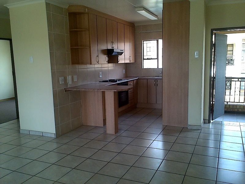 A functional kitchen featuring light wood cabinetry, tiled flooring, built-in oven and hob, and a breakfast counter, offering a clean and practical workspace.
