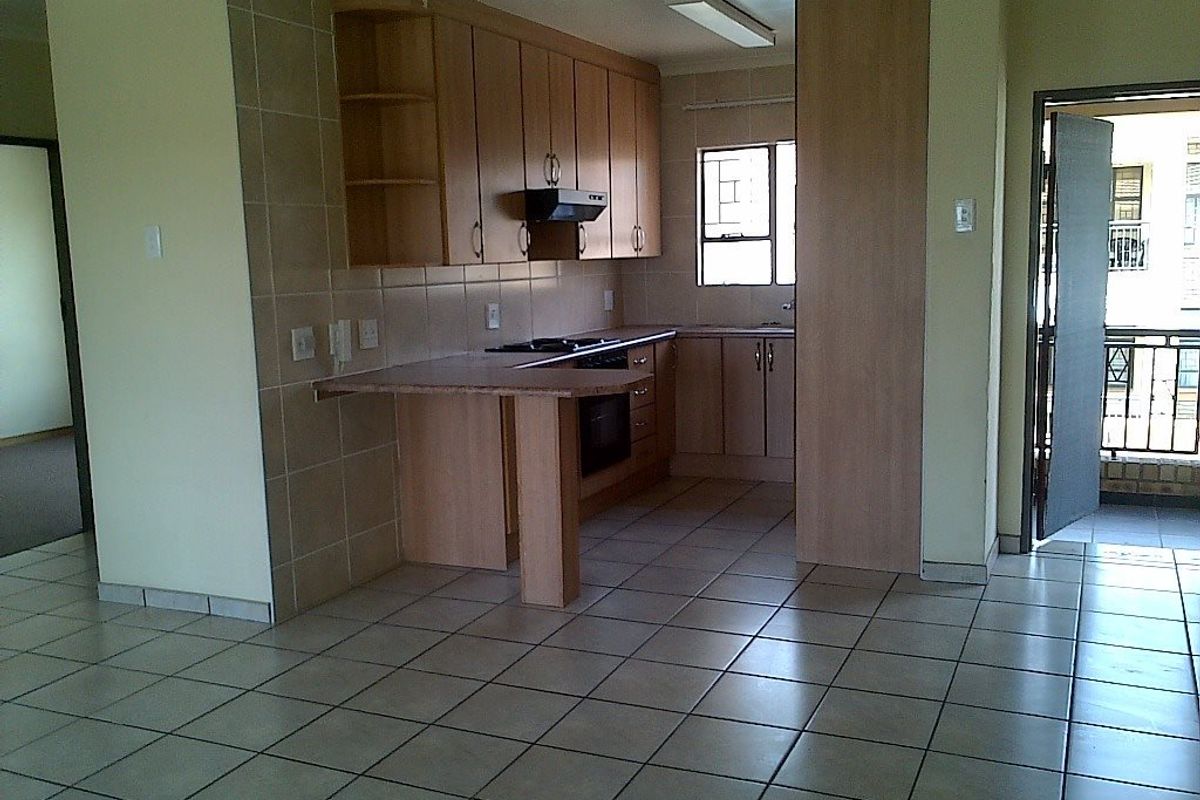 A functional kitchen featuring light wood cabinetry, tiled flooring, built-in oven and hob, and a breakfast counter, offering a clean and practical workspace.