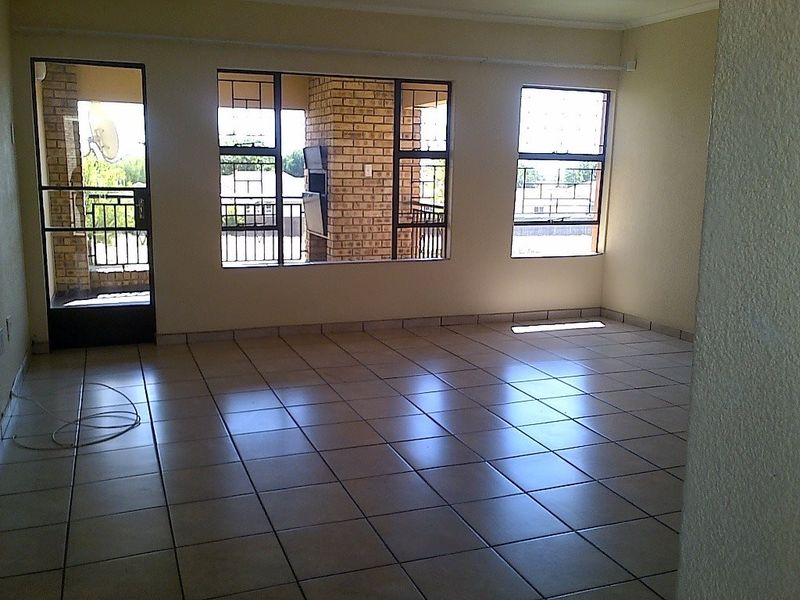 An empty, tiled living area featuring large windows and a security gate leading to an outdoor patio space.