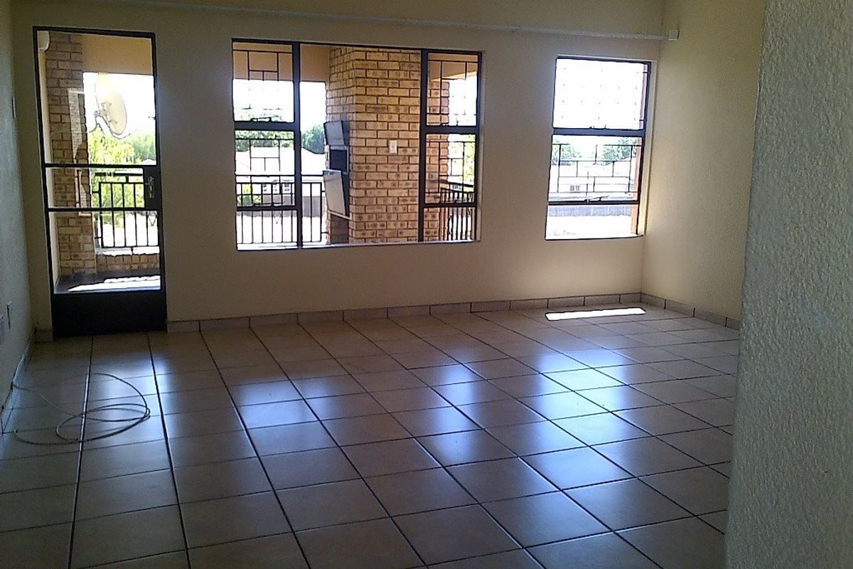 An empty, tiled living area featuring large windows and a security gate leading to an outdoor patio space.