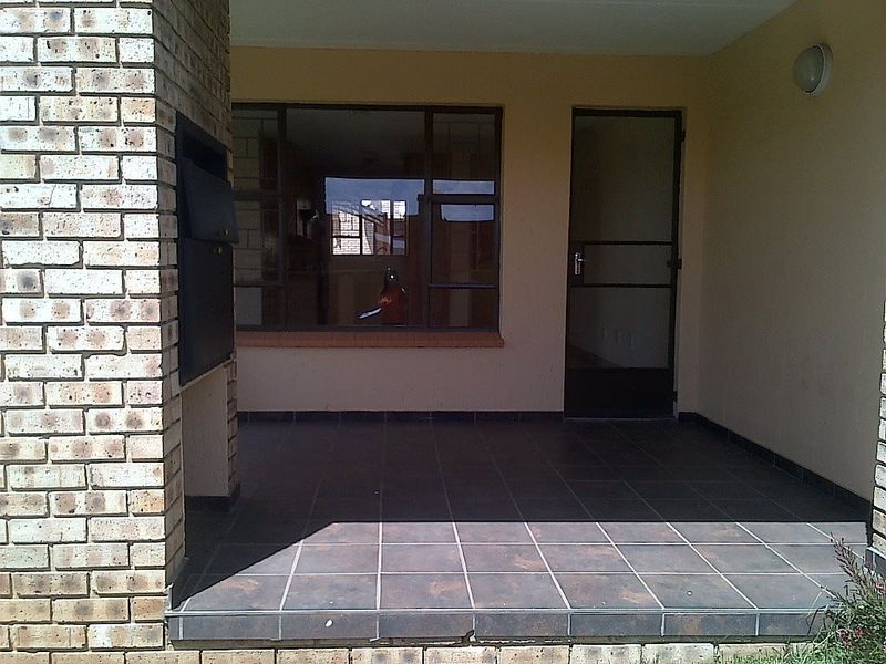 Covered patio area featuring a built-in braai, tiled flooring, and direct access to the home through a security gate.