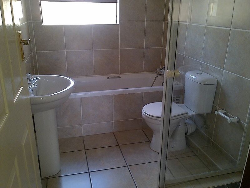 A functional bathroom featuring a pedestal basin, bathtub, and toilet with neutral wall and floor tiling.