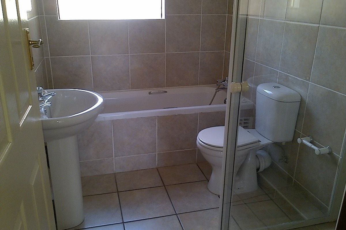 A functional bathroom featuring a pedestal basin, bathtub, and toilet with neutral wall and floor tiling.
