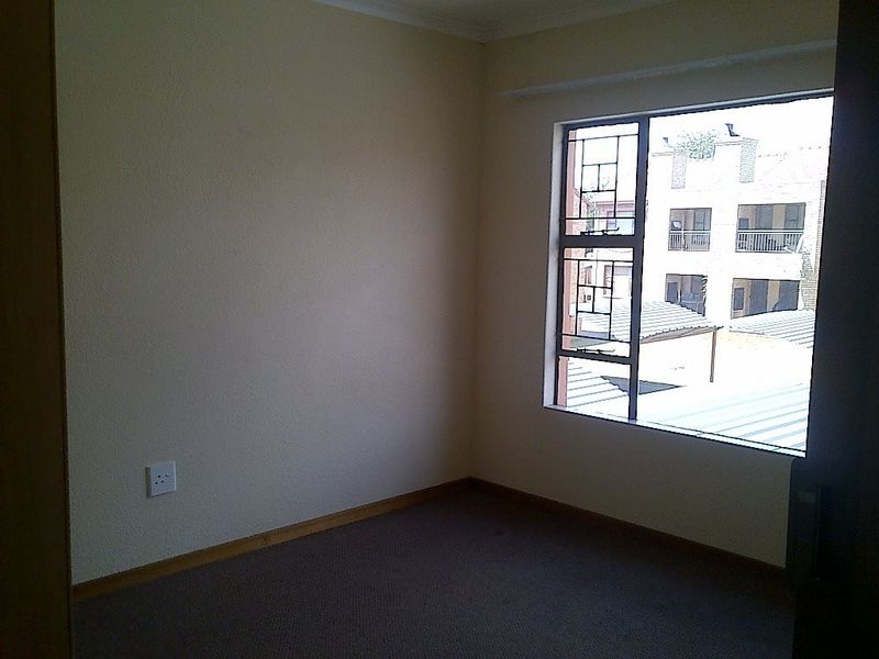 An empty bedroom featuring carpeted flooring and a metal-framed window with views of the surrounding complex.