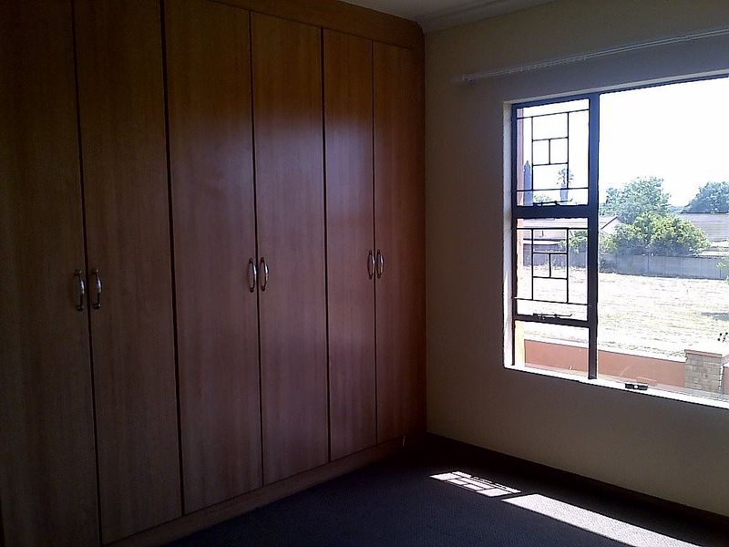 A spacious bedroom featuring extensive built-in wooden cupboards and a window with security bars, offering a clean and functional living space.