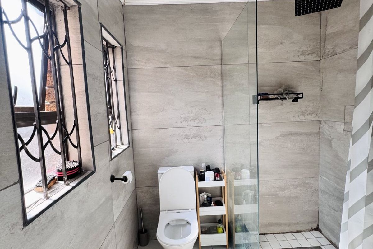 Modern bathroom featuring large-format grey wall tiles, a glass-enclosed walk-in shower with a rainfall showerhead, and a white toilet.