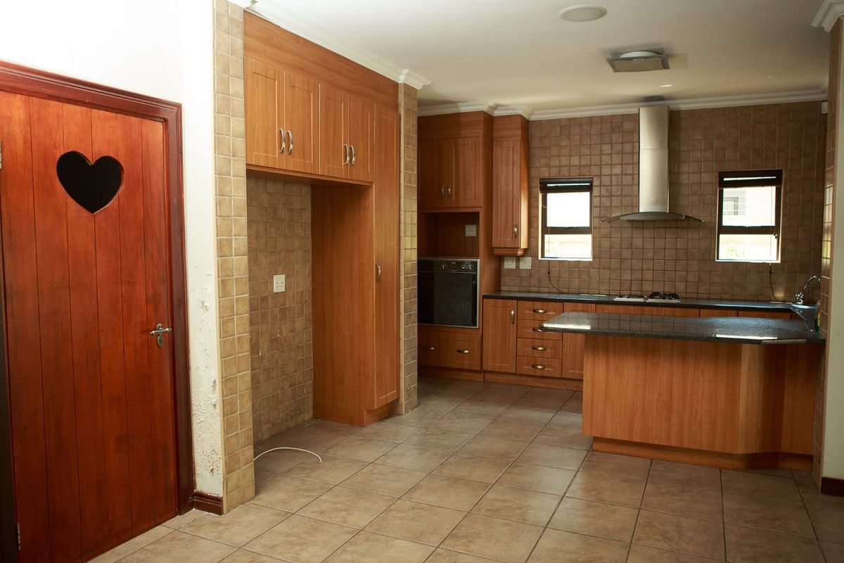 Spacious kitchen featuring wooden cabinetry, granite countertops, built-in oven, and stainless steel extractor fan, offering a functional layout with tiled finishes throughout.