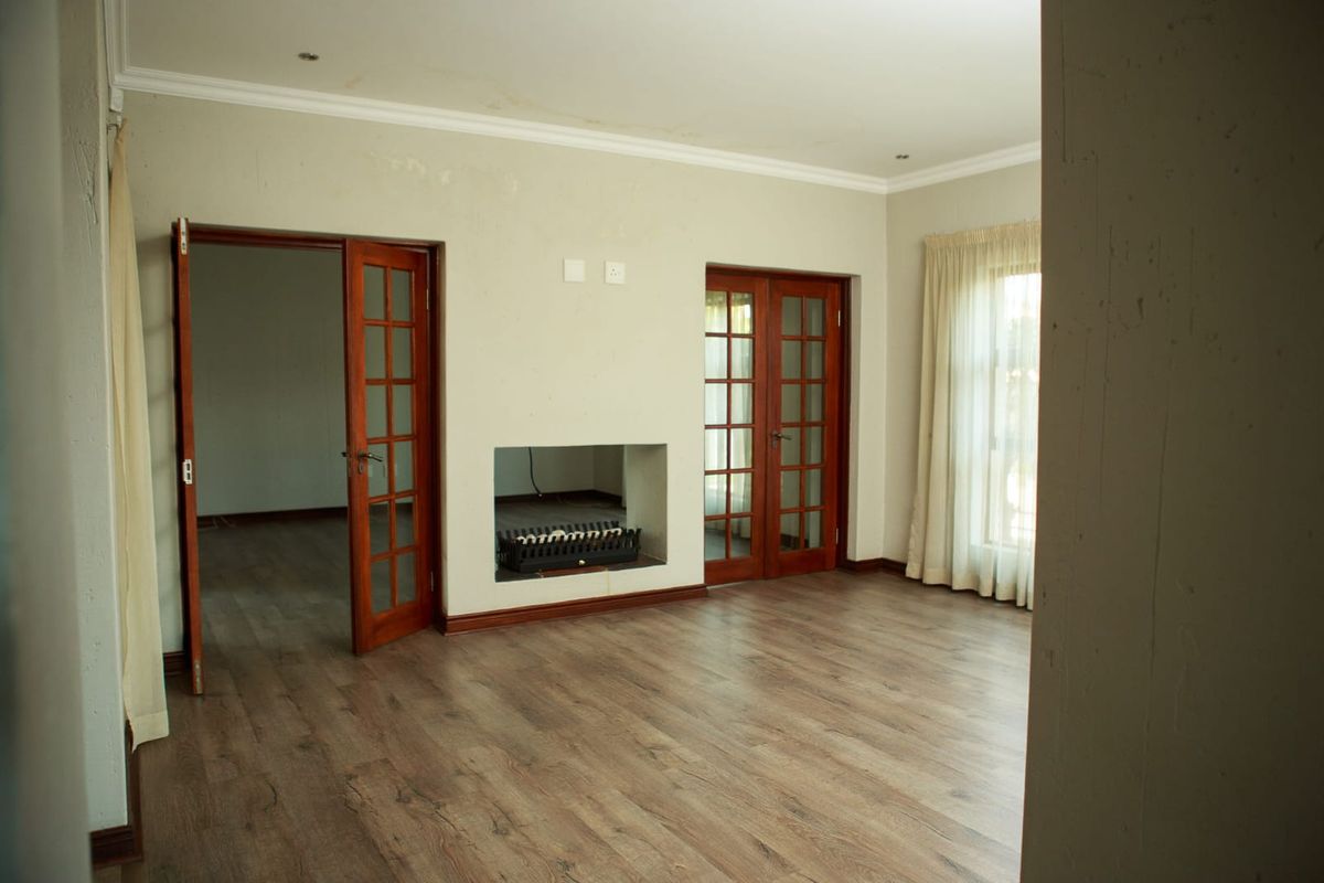 Spacious living room featuring laminate flooring, a built-in fireplace, and classic wooden french doors leading to adjacent areas.