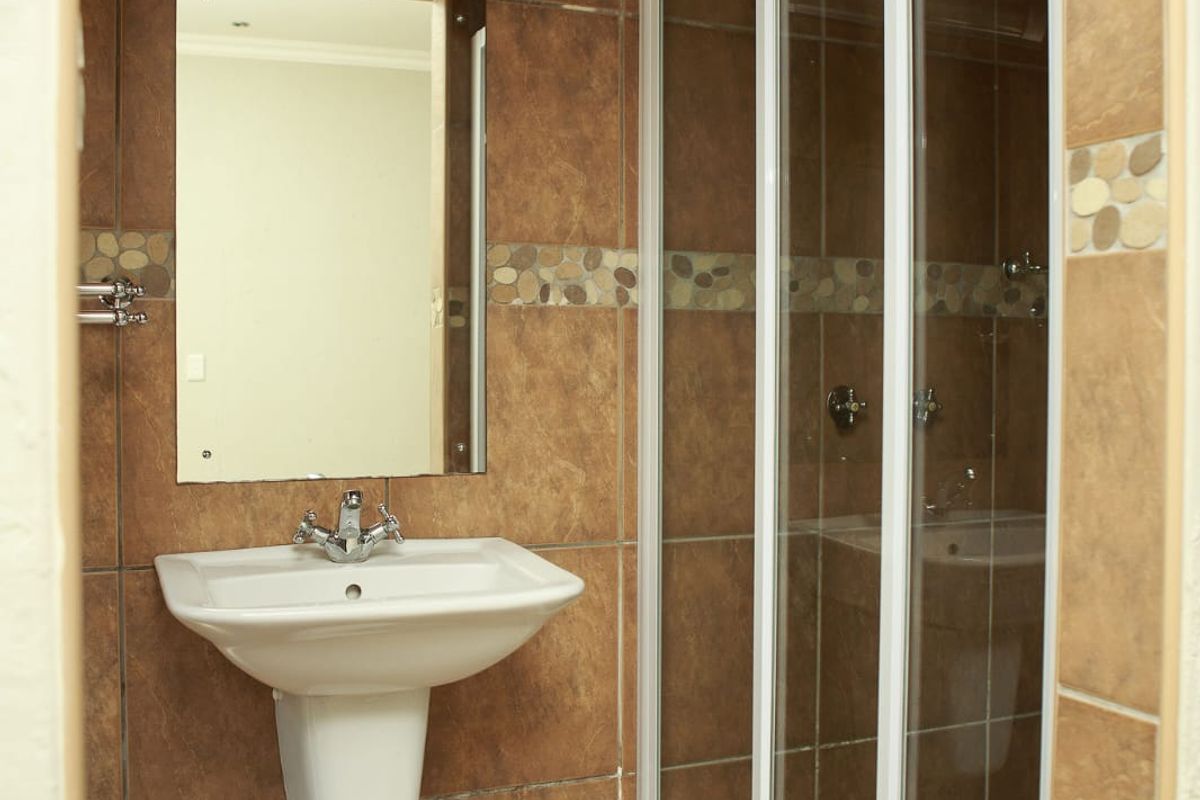 A functional bathroom featuring a pedestal washbasin, a glass-enclosed shower, and brown ceramic tiling throughout.