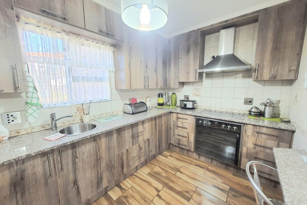 A functional kitchen featuring wood-look cabinetry, granite countertops, a built-in oven with extractor fan, and durable tiled flooring.