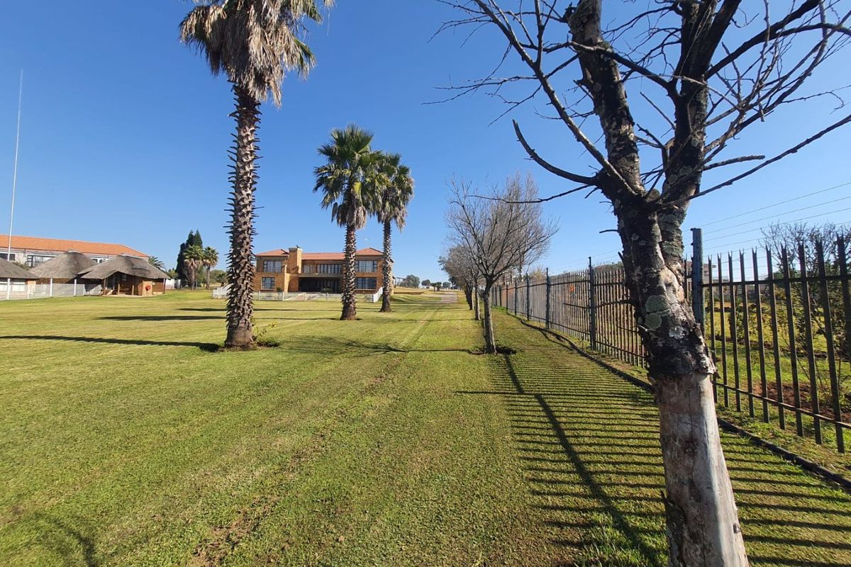 A wide-angle view of a spacious farm property featuring a large manicured lawn, mature palm trees, and secure metal perimeter fencing.